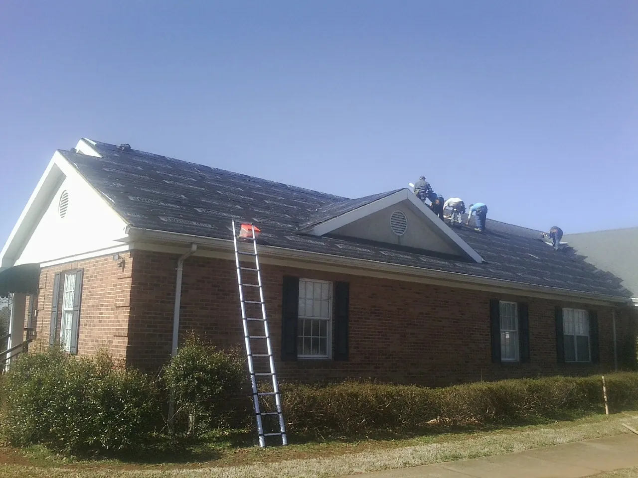 Crew tearing shingles off a brick ranch roof with a ladder set — Metal Roof Repair work by our crew in Lewisburg