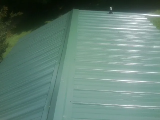 New green metal panels meeting at the ridge of a roof — Flat Roof Repair work by our crew in Lewisburg