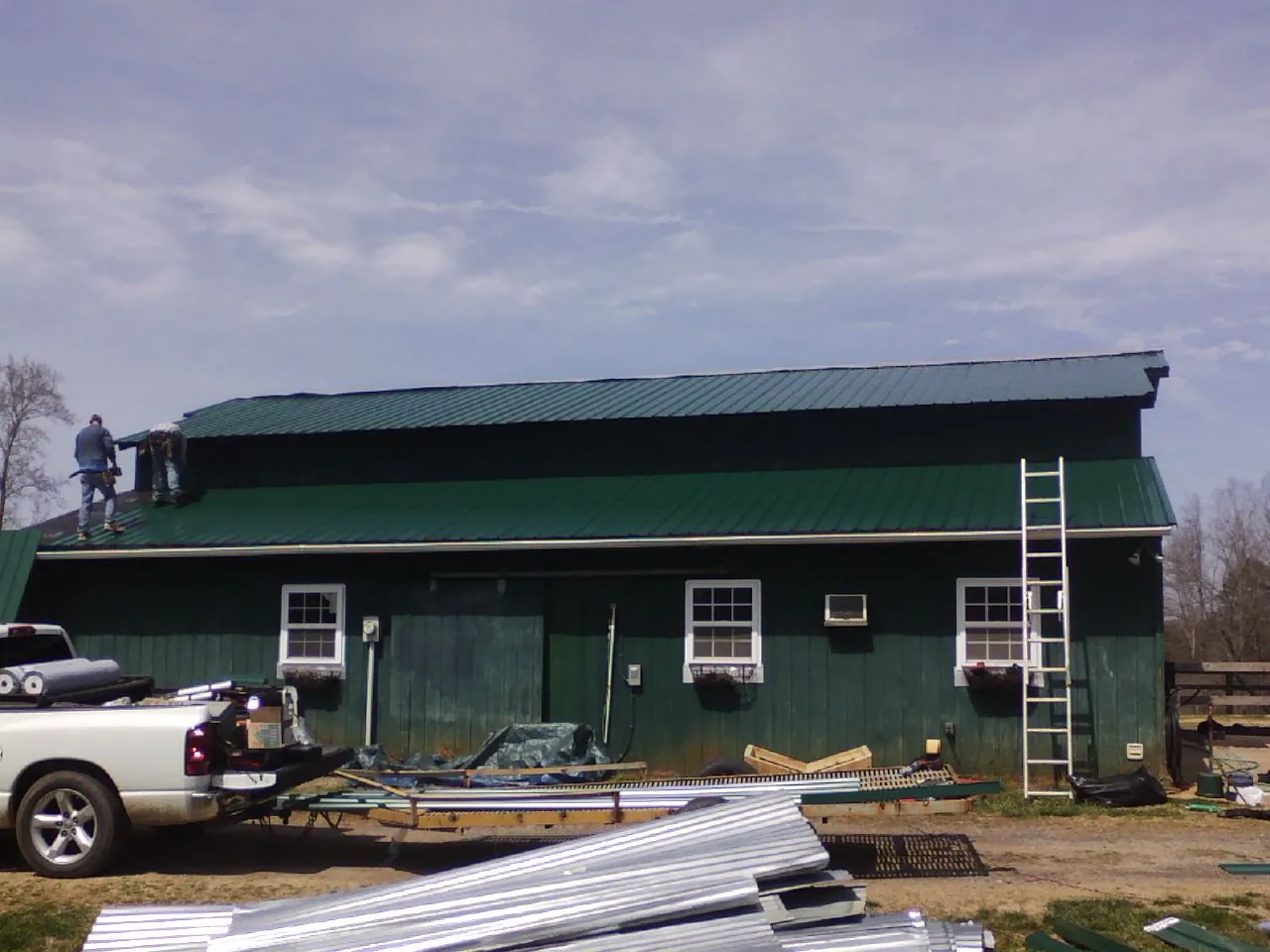 Crew installing green metal roofing on a large green barn in Lewisburg
